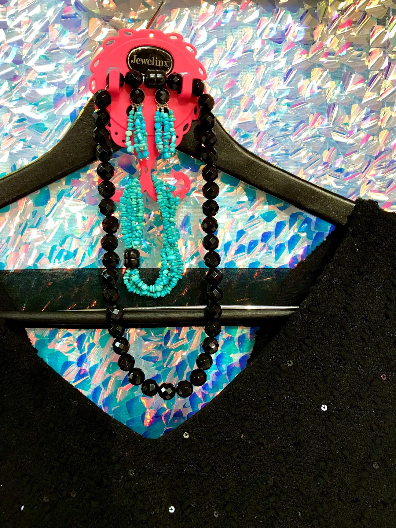 Hot Pink Jewelinx hanging jewelry organizer holding turquoise and black beaded necklaces and earrings, paired with a black sequin top